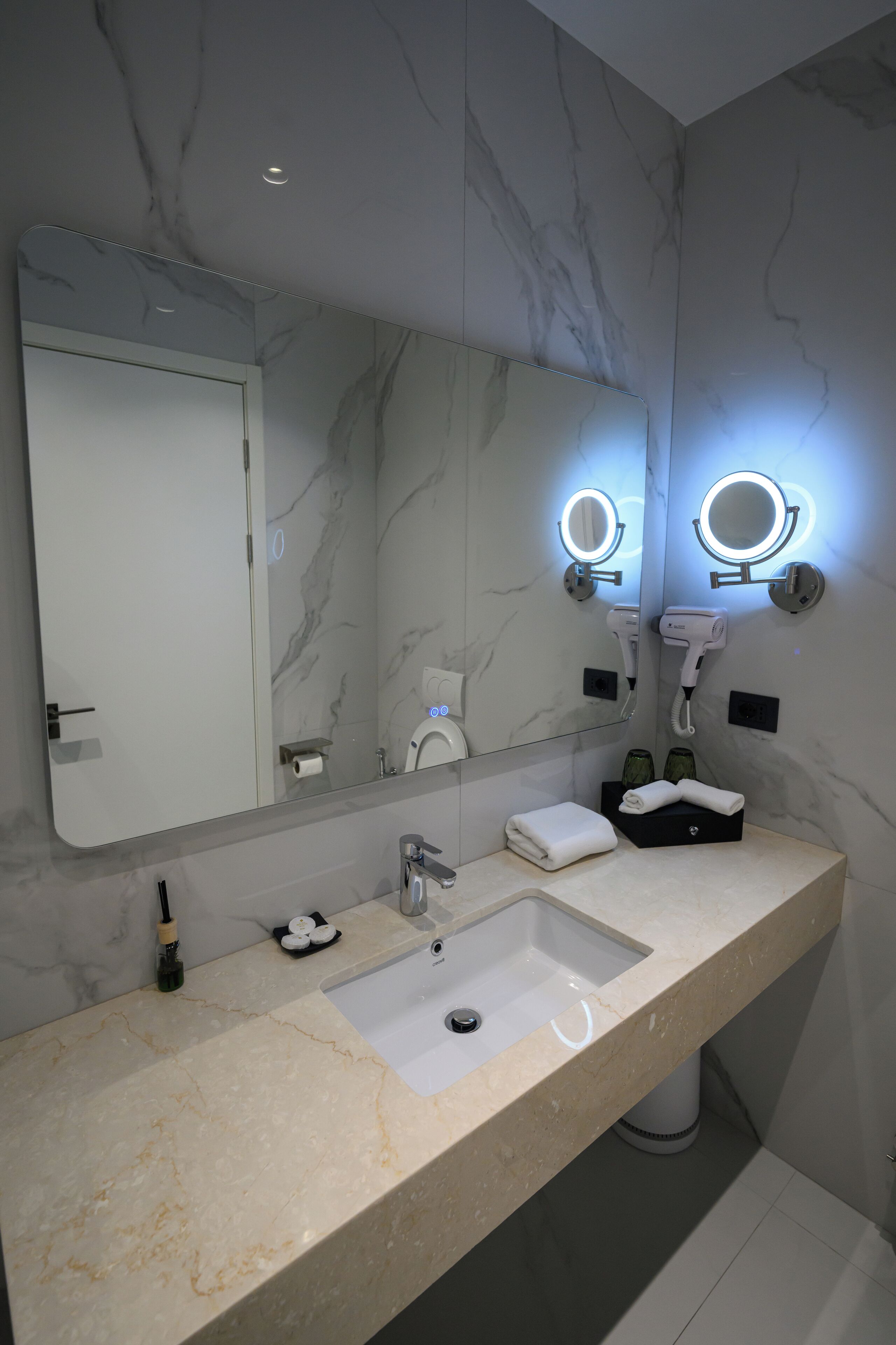 A modern bathroom with a marble vanity, a large mirror, and two illuminated vanity lights.