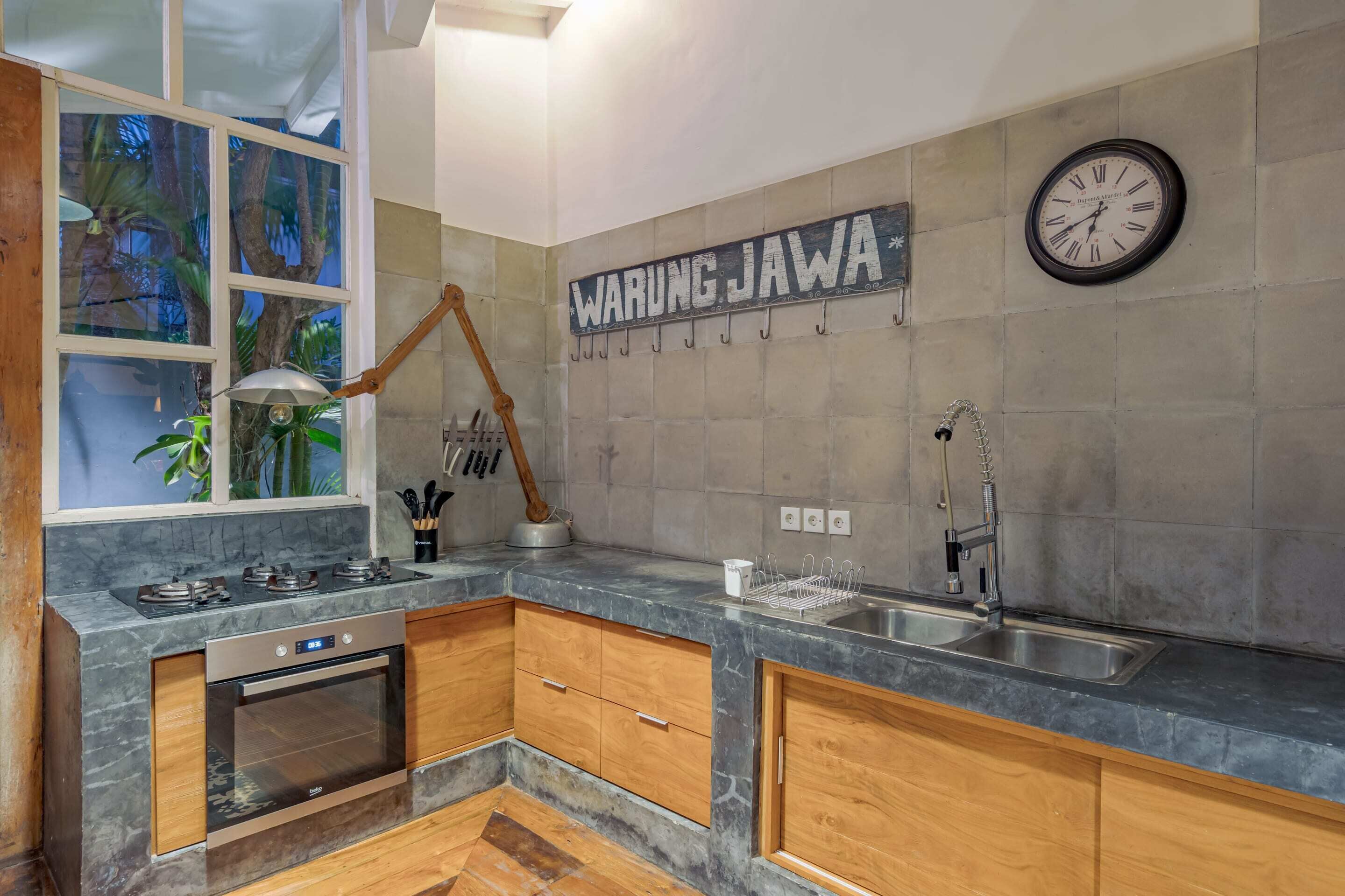 Una cocina moderna con encimera de mármol, armarios de madera, horno empotrado, un lavabo y un reloj de pared.