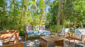 Une terrasse en bois agrémentée d’un canapé, de fauteuils et d’une table basse, le tout entouré d’une végétation tropicale luxuriante.