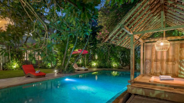 Un espace piscine doté d’une terrasse en bois, de chaises longues et d’une pergola illuminée de guirlandes lumineuses.