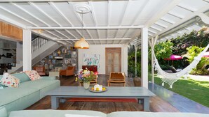 Un salon moderne avec un canapé, une table basse et des fauteuils, un escalier et un hamac dans un jardin.