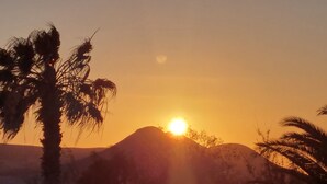 A sunset over a mountainous landscape with palm trees. - Studio With Pool, Garden and Open Roof Bathroom (La Oliva)