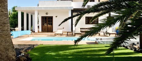 Een modern huis met een zwembad, een overdekt terras en een verzorgd gazon.