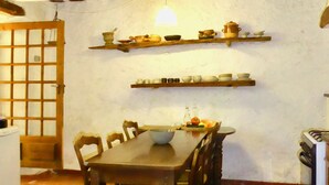 Un comedor con una mesa y sillas de madera, una lámpara colgante y estantes con vajilla.