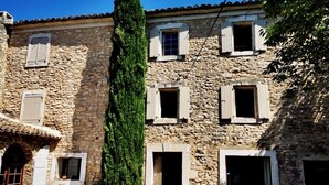 Un edificio de piedra con varias ventanas y puertas, un árbol alto en primer plano y un camino adoquinado.