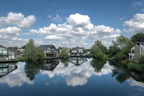 A tranquil lakeside residential area with modern houses, a clear sky, and calm water reflecting the surroundings.