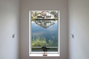 A room with a large window overlooking a body of water and a house across the water.
