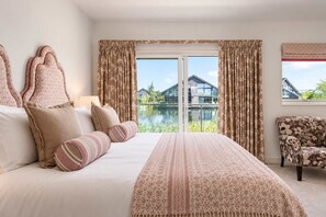 A bedroom with a large bed, a chair, and a view of a house through a window.