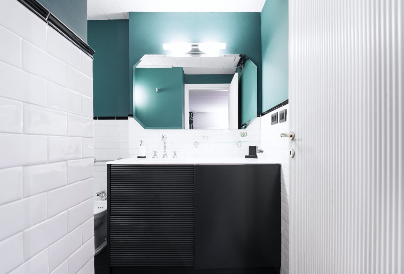Un baño moderno con paredes de azulejos blancos, un tocador negro y una pared de acento color verde azulado.