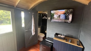 A compact bathroom with a wooden ceiling, a toilet, a sink, and a small cabinet with a television mounted above it. - Enchanted Cabin Retreat in Sibford Gower (Banbury)
