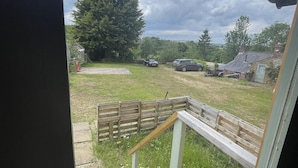 A view from a window overlooking a grassy yard with a wooden fence, a wooden staircase, and a parked car. - Enchanted Cabin Retreat in Sibford Gower (Banbury)