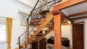 Una escalera de madera con barandillas de metal, un comedor con mesas y sillas redondas, y un sofá.