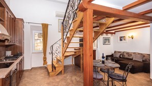 Una cocina con armarios de madera, un comedor con mesa y sillas, una escalera con barandilla de madera y una sala de estar con sofá y cojines.