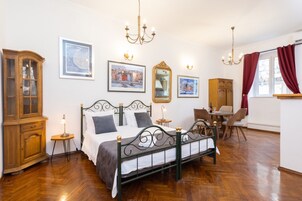 Quarto com cama, aparador de madeira, mesa de jantar, cadeiras e obras de arte nas paredes.