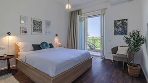 Un dormitorio con cama, mesitas de noche, una silla, una planta en maceta y un balcón con vistas.