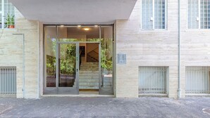 Una entrada de edificio con puerta de cristal, una escalera que da al interior y una reja metálica a la izquierda.