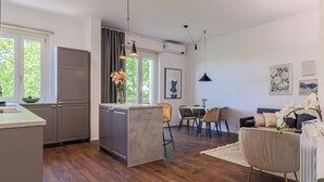 Una cocina moderna con una isla central, comedor con sillas y sala de estar con sofá y elementos decorativos.