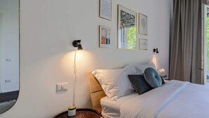 Un dormitorio con cama, lámparas de noche, un interruptor de luz en la pared y cuadros enmarcados.