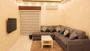 Una sala moderna con un sofá seccional, una mesita blanca y un ventanal con persianas horizontales.