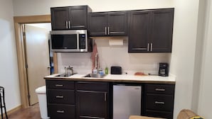 A compact kitchen with dark cabinets, a microwave, a refrigerator, and a coffee maker. - Hazel Suite - Homer Seaplane Base (Homer)