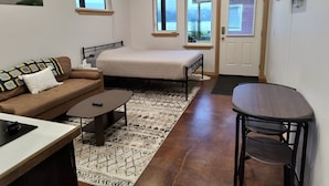 A compact room with a bed, a sofa, a small table, and a TV mounted on the wall. - Hazel Suite - Homer Seaplane Base (Homer)