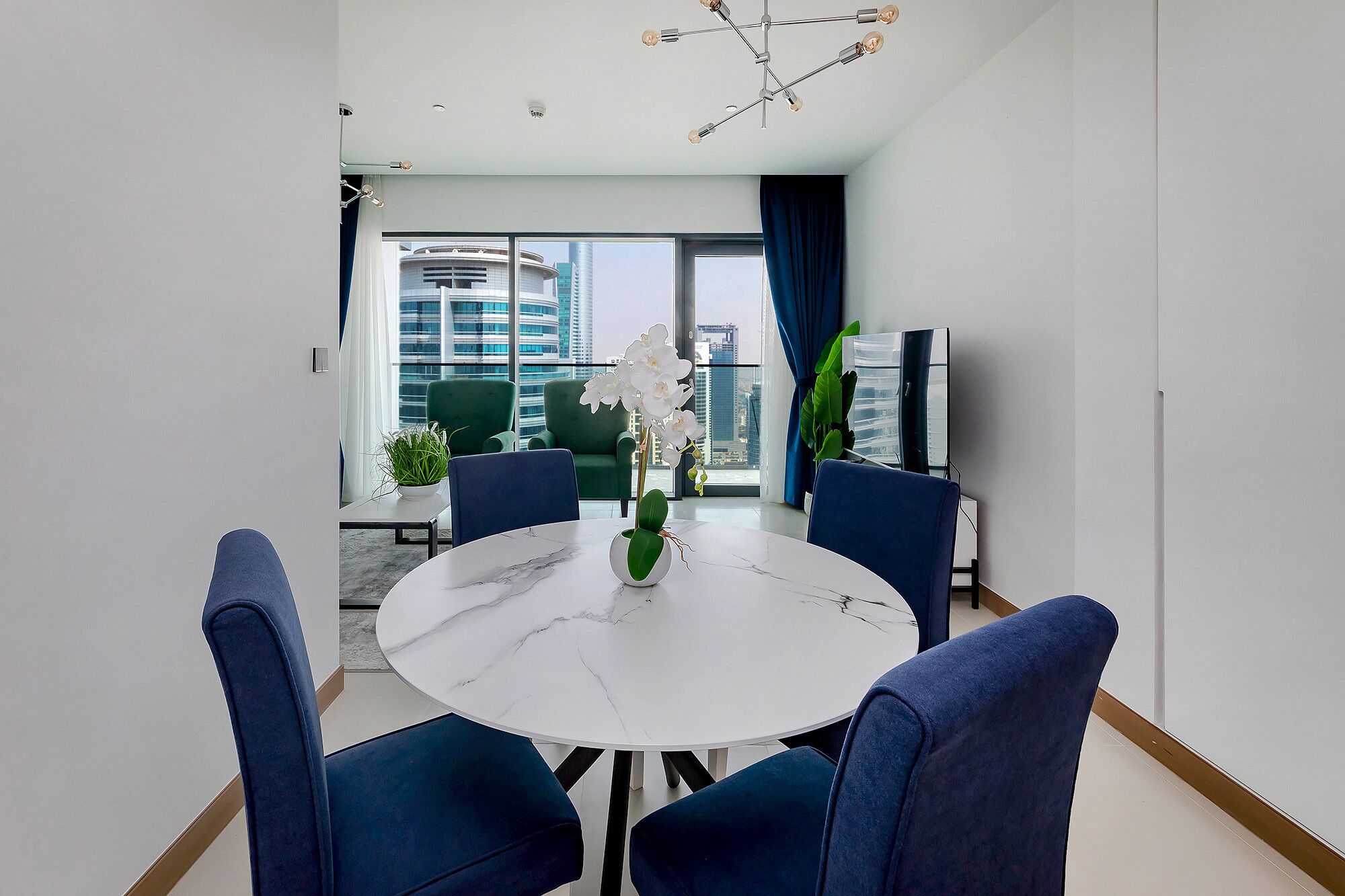 A modern dining area with a round table, blue chairs, and a vase of white flowers.