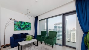 Un salon moderne avec vue sur la ville, un canapé bleu, des fauteuils verts, une table basse blanche et une grande fenêtre ornée de rideaux bleus.