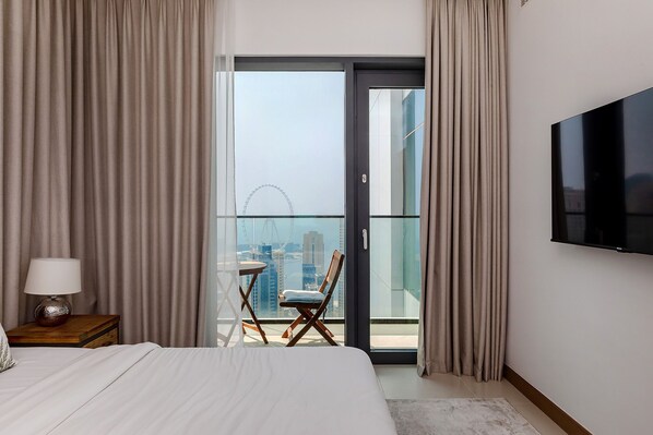 A hotel room with a bed, a TV, a nightstand, a lamp, a chair, and a balcony with a city view. - Stylish 2BR with Marina Views (Dubai)