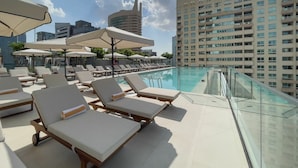 Un espace piscine aménagé sur le toit, avec des chaises longues et des parasols, entouré de grands immeubles.