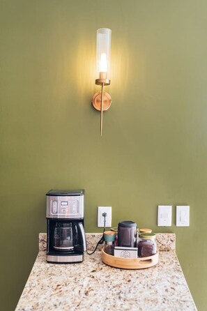 A kitchen area with a coffee maker, a kettle, and a jar on a countertop.