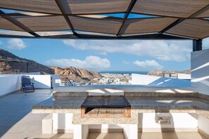 A rooftop terrace with a view of a city and mountains, a lounge chair, and a table.