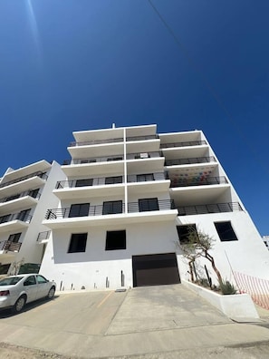 A multi-story building with a flat facade, balconies, and a car parked in front.