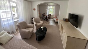 A modern living room with a sofa, chairs, a coffee table, a TV, and a dining area with a table and chairs. - Ruhige Unterkunft für 2-3 Personen in Bad Salzungen (Bad Salzungen)