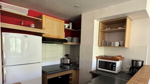 Una cucina compatta con frigorifero, fornello, microonde e lavello. Dispensa con mobili in legno e parete rivestita in piastrelle.
