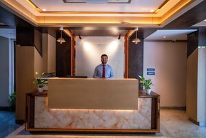 A reception desk with a marble top, wooden paneling, and two potted plants.
