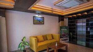A lobby with a yellow sofa, a wooden coffee table, a potted plant, a framed picture on the wall, and an elevator. - Evara Hills, Gangtok (Gangtok)