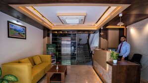 A reception area with a wooden reception desk, a yellow sofa, a small wooden table, and a staircase in the background. - Evara Hills, Gangtok (Gangtok)