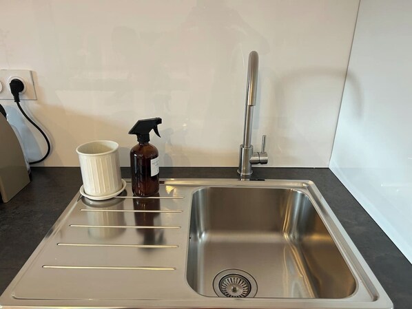 A stainless steel kitchen sink with a faucet, a white cup, and a spray bottle on the countertop.