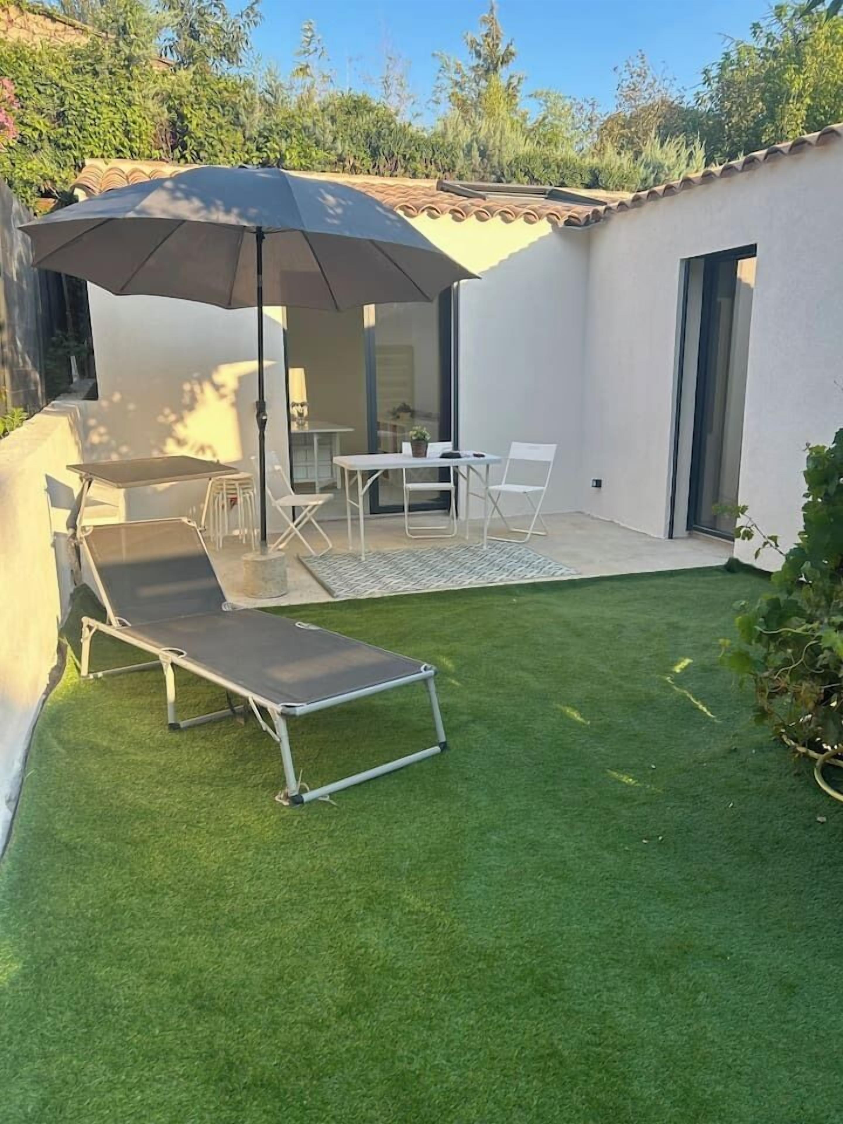 Un patio con una mesa y sillas, una tumbona y un gran paraguas.