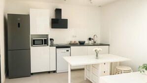A modern kitchen with a refrigerator, microwave, dishwasher, and a white dining table. - House Garden Pool – The Cherry Tree (Venelles)