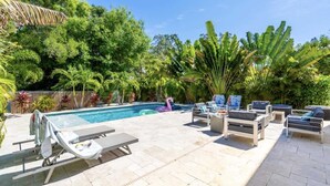 A poolside area with lounge chairs and a swimming pool surrounded by lush greenery. - Arlington Ocean Oasis 5br 5ba Htd Saltwater Pool (Sarasota)