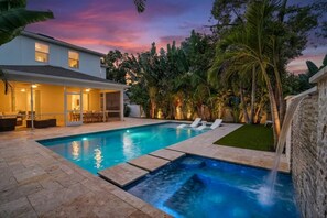 Una piscina con cascada, rodeada de un patio amoblado con mobiliario exterior.