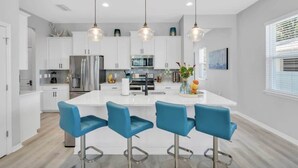 A modern kitchen with white cabinets, stainless steel appliances, and blue bar stools. - Arlington Ocean Oasis 5br 5ba Htd Saltwater Pool (Sarasota)