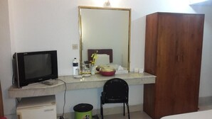 Una camera d'albergo con televisore, uno specchio, un armadio in legno, una scrivania con sedia e un piccolo cestino.