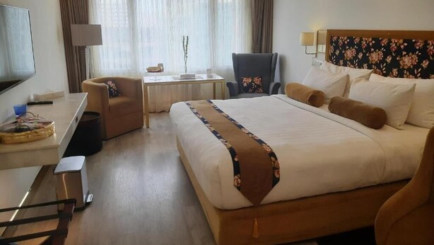 Camera d'albergo con un letto grande, una scrivania, una sedia, una televisione e una finestra con tende.