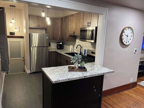 A modern kitchen with stainless steel appliances, wooden cabinets, and a granite countertop. - Revitalized Mid-Century Modern Gem (Sioux Falls)