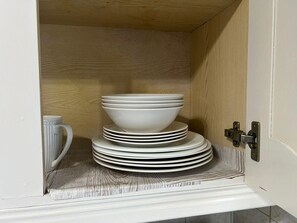 Un armario con una pila de platos blancos y una taza blanca.