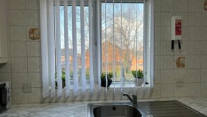 A kitchen with a sink, a window with blinds, and a fire blanket on the wall. - Birmingham Luxury House - Modern Retreat (Birmingham)