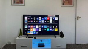 A flat-screen TV on a white entertainment unit with a remote control and a small plant beside it. - Birmingham Luxury House - Modern Retreat (Birmingham)