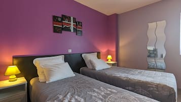A room with two beds, a nightstand with a lamp, a wall with artwork, and a decorative mirror.
